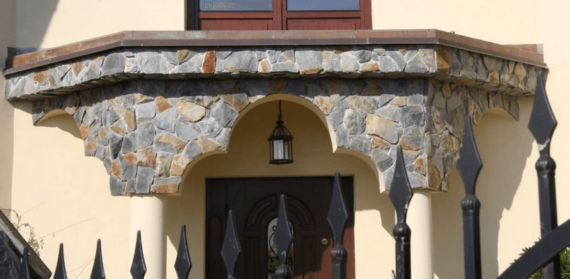Stone facade with arched doorway, lantern, and dark wrought iron fence.