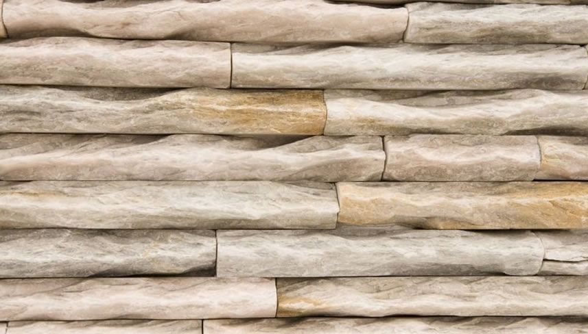 Close-up of a stacked stone wall in varying shades of beige and tan.