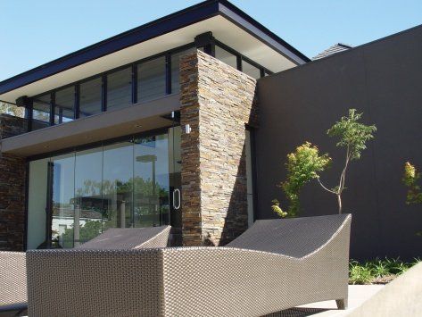 Modern building with glass walls, stone accents, and lounge chairs. Sunny outdoor setting.