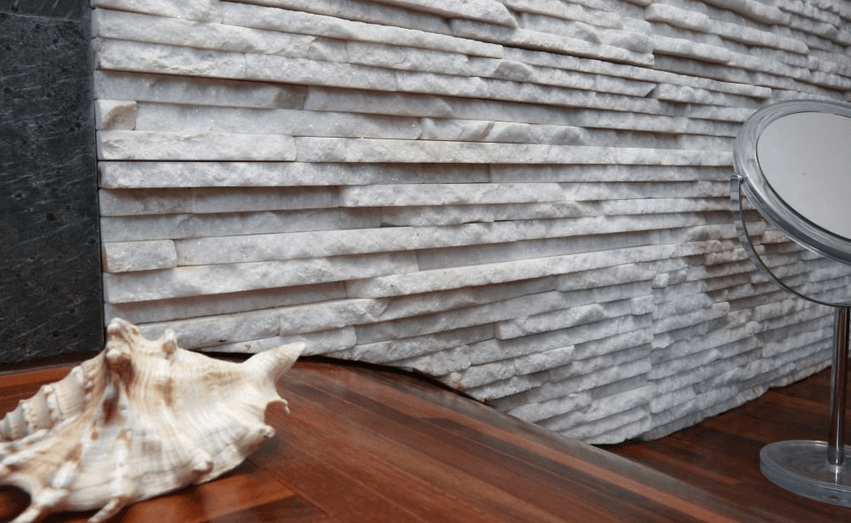 White stacked stone wall with a seashell and mirror on a wooden surface.