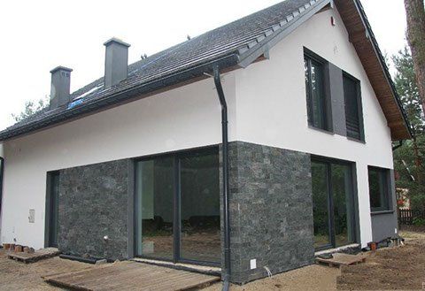 Modern two-story house with white walls, dark gray stone accent, large sliding glass doors, and dark roof.