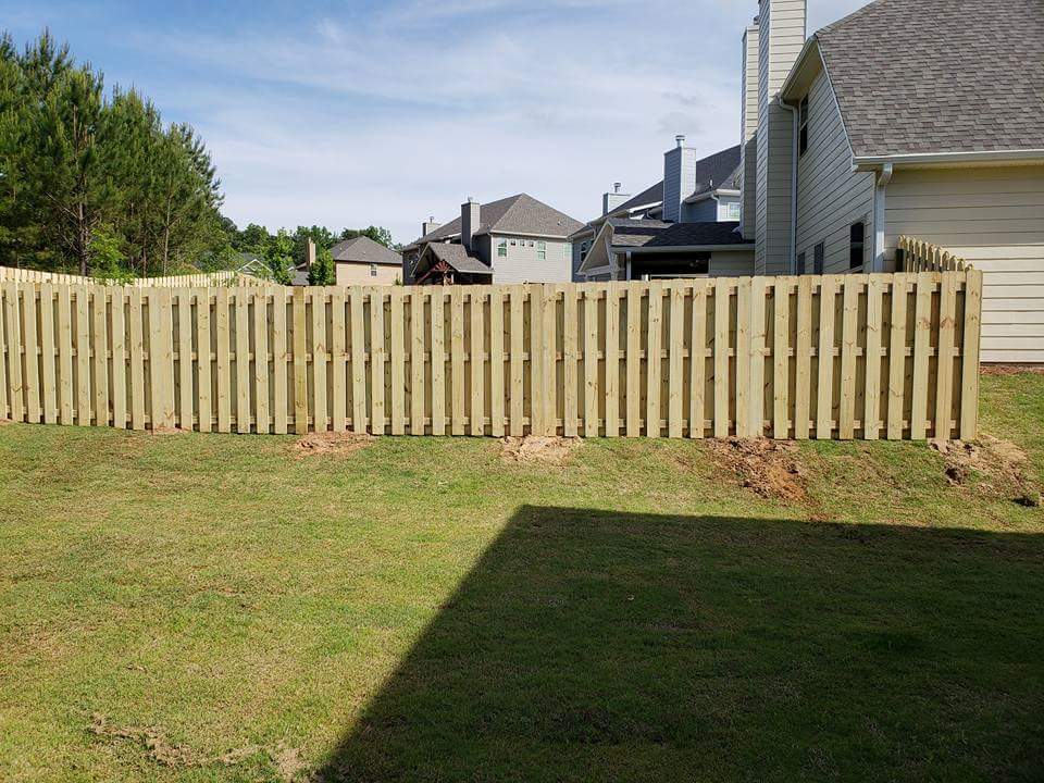 A wooden fence is in the backyard of a house.