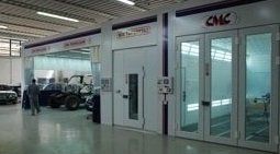 Interno di una concessionaria o di un'officina con ingresso in vetro, veicoli parcheggiati e pavimenti bianchi luminosi.