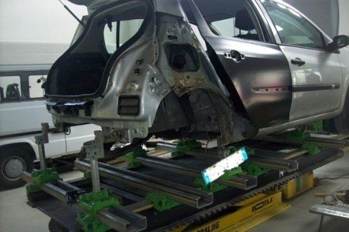 Auto argentata danneggiata su un telaio idraulico in un'officina di riparazione auto.