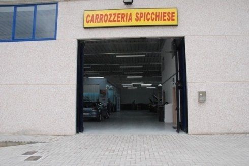 Ingresso del garage aperto con insegna “Carrozzeria Spicchese” sopra la porta.