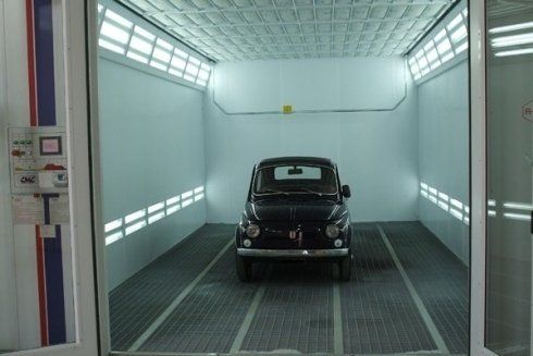 Auto d'epoca nera all'interno di una cabina di verniciatura bianca, vista frontalmente.