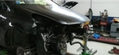 Una motocicletta nera in un garage, con la carenatura anteriore rimossa, che lascia intravedere le parti esposte vicino a un banco da lavoro.