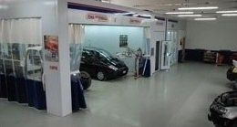 Interno di una concessionaria con diverse auto in esposizione e personale in piedi vicino a un veicolo nero.