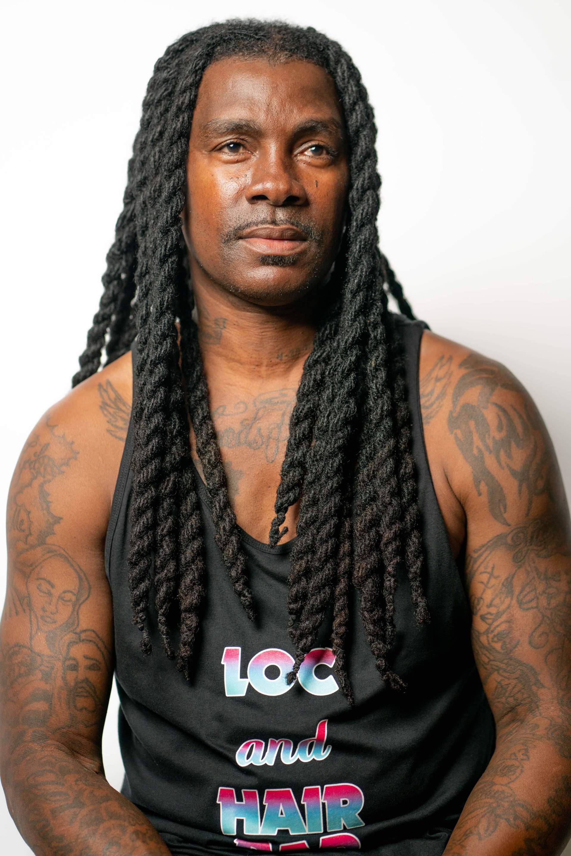 Portrait of a man with long braids wearing a black tank top against a white background