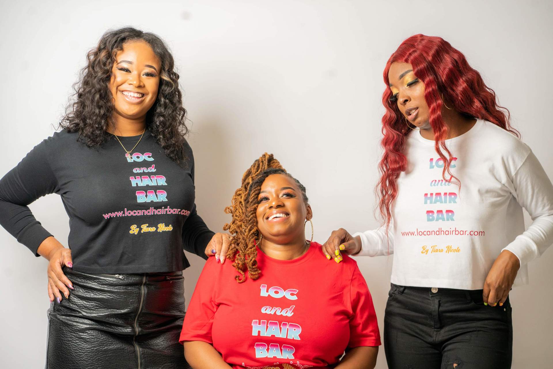 Three women posing in branded sweatshirts, smiling against a white backdrop.