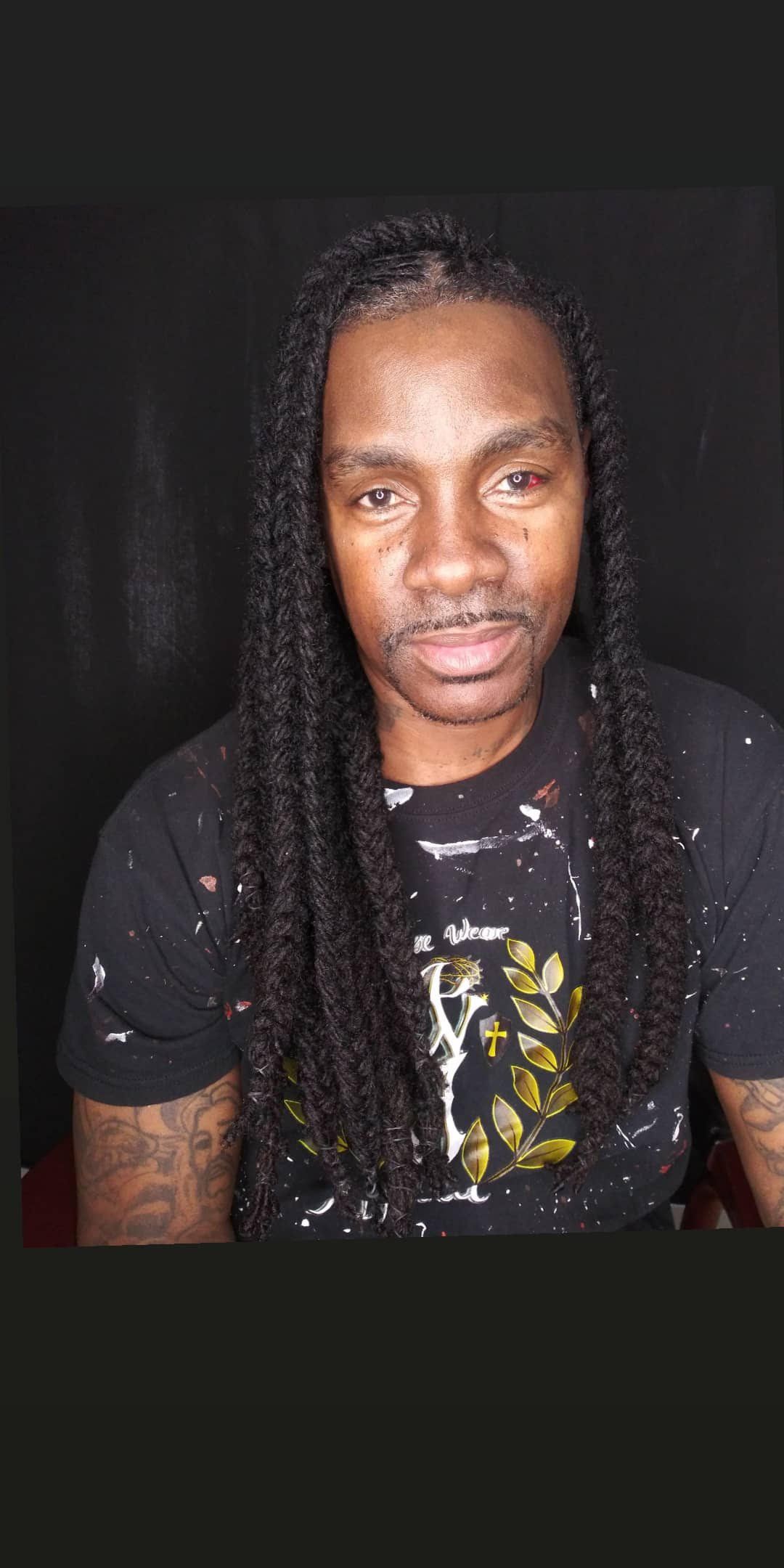 Portrait of a person with long braided hair wearing a black shirt against a dark background