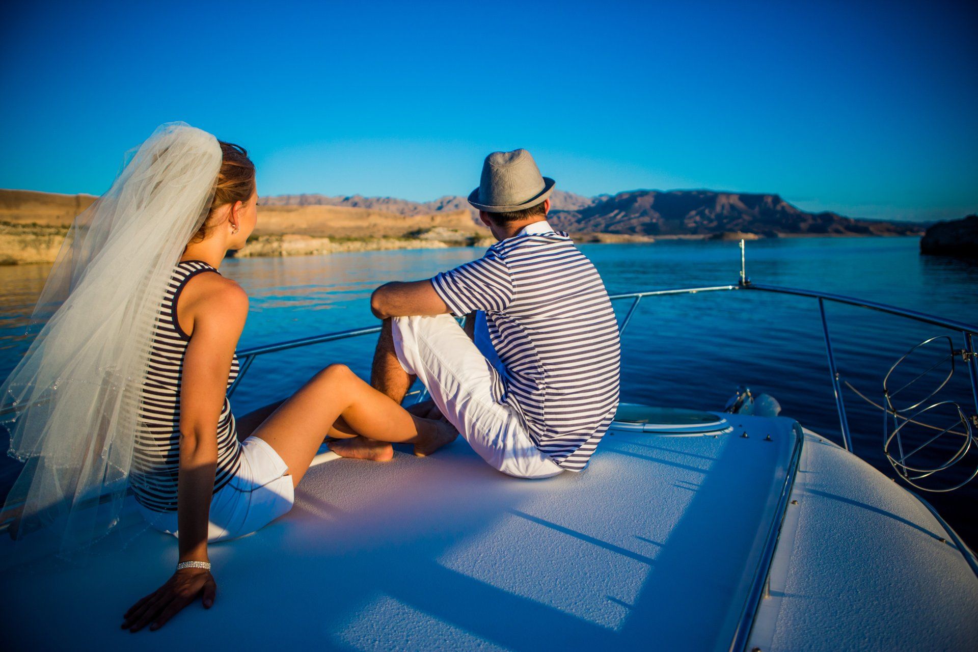A bride and groom are sitting on the back of a boat looking at the water.