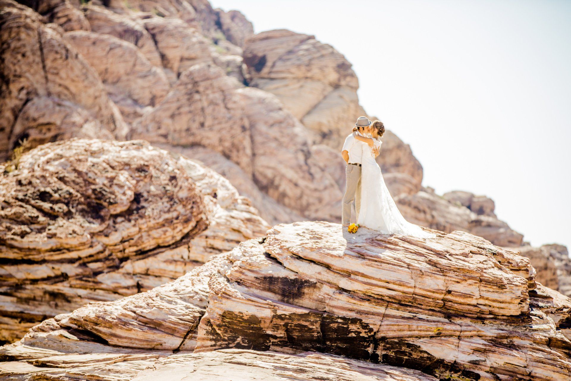 A bride and groom are kissing on top of a rocky mountain.
