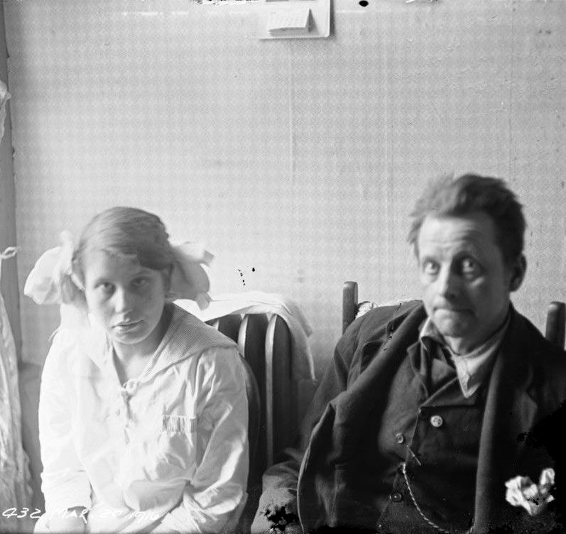 A young man and woman with intellectual disabilities living in slum housing in Toronto. The young woman has blonde hair styled in two ponytails and is wearing a sailor style blouse. The young man has dark messy hair and is wearing a rumpled three piece suit. Images like this were taken by the Toronto Department of Health and used as eugenics propaganda by organizations like the Canadian National Committee for Mental Hygiene (today the Canadian Mental Health Association). This propaganda was designed to convince the public that those deemed disabled were a threat to society which must be eliminated. A young man and woman with intellectual disabilities living in slum housing in Toronto. The young woman has blonde hair styled in two ponytails and is wearing a sailor style blouse. The young man has dark messy hair and is wearing a rumpled three piece suit. Images like this were taken by the Toronto Department of Health and used as eugenics propaganda by organizations like the Canadian National Committee for Mental Hygiene (today the Canadian Mental Health Association). This propaganda was designed to convince the public that those deemed disabled were a threat to society which must be eliminated.