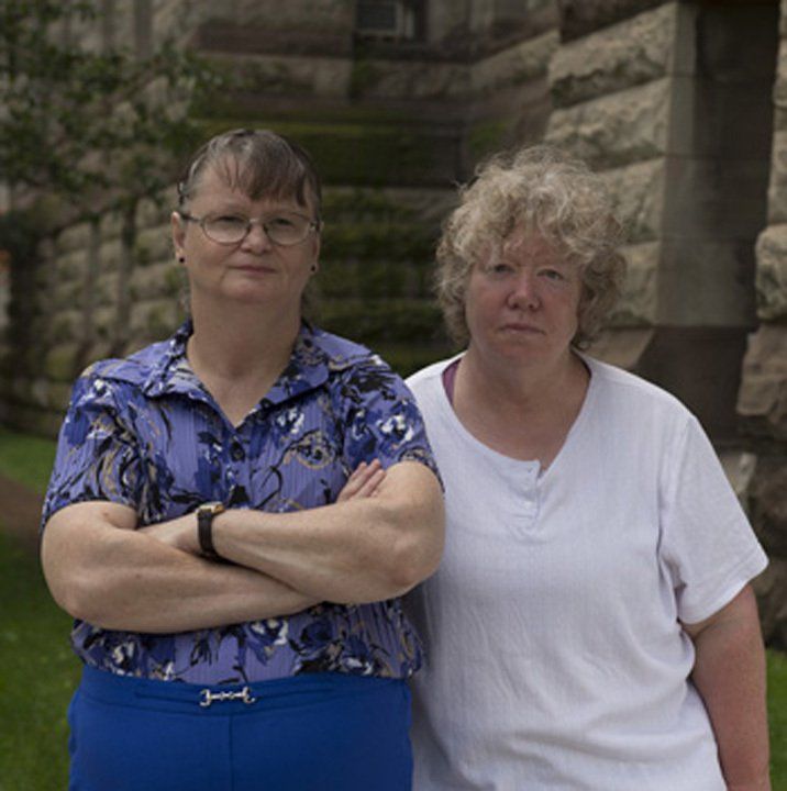 An image of Pat Seth (right) and Marie Slark (left), the two representative plaintiffs in the Huronia Regional Centre class action lawsuit. Marie is dark haired woman with oval wire-rimmed glasses and she wears blue slacks and a purple-blue button up short sleeve shirt. Pat is a woman with short curly blonde hair and she wears a white short sleeve shirt. Image from an issue of Canada’s History Magazine. An image of Pat Seth (right) and Marie Slark (left), the two representative plaintiffs in the Huronia Regional Centre class action lawsuit. Marie is dark haired woman with oval wire-rimmed glasses and she wears blue slacks and a purple-blue button up short sleeve shirt. Pat is a woman with short curly blonde hair and she wears a white short sleeve shirt. Image from an issue of Canada’s History Magazine.