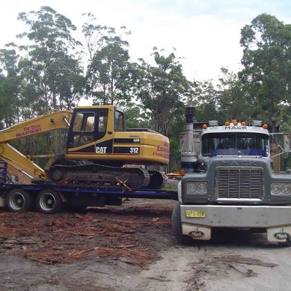 Site preparation yellow bob cat being hauled by a large truck
