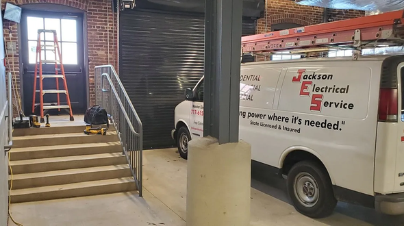 A white van with the label Jackson Electrical Service Truck parked in front of a brick house