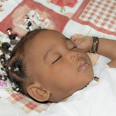 A baby with braids sleeping on a blanket