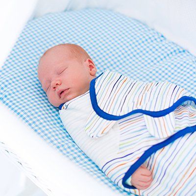 A baby wrapped in a striped blanket is sleeping on a bed.