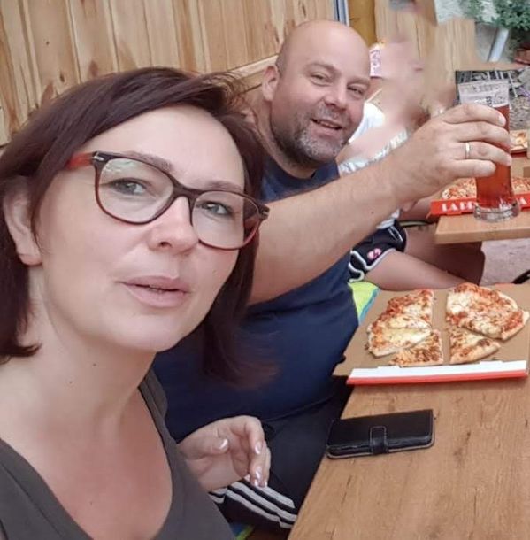 Twee mensen zitten aan een tafel en delen pizza en drankjes, terwijl ze glimlachen in een informele restaurantomgeving.