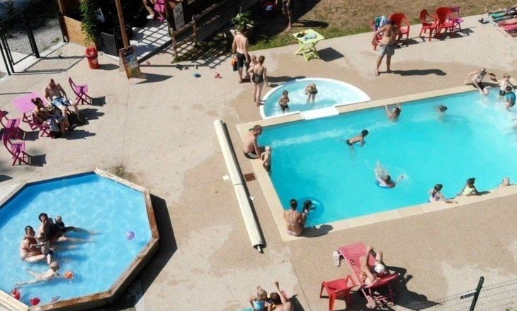 Buitenzwembad met mensen die ontspannen en zwemmen, inclusief een jacuzzi en ligstoelen.
