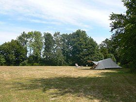 Tent en campingstoelen op een grasveld onder een blauwe hemel, met bomen op de achtergrond.
