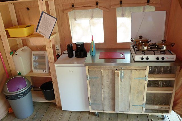 Compacte keuken in een houten blokhut met fornuis, spoelbak, koelkast, planken en kookgerei.