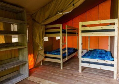 Stapelbedden in een knusse tent met houten vloer en blauw beddengoed.