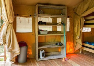 In een beige tent staat een metalen rek met benodigdheden naast een vuilnisbak en een waterkoker.