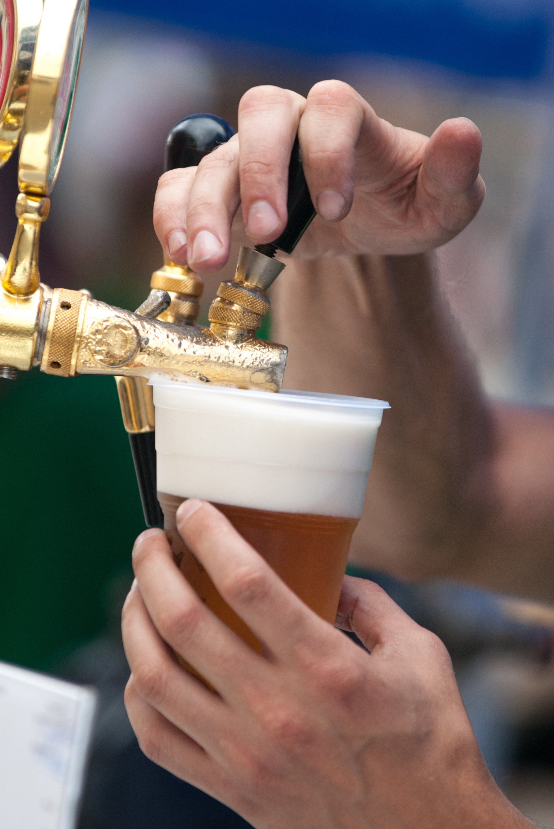 Hands pouring beer from a tap into a plastic cup, creating a foamy head.