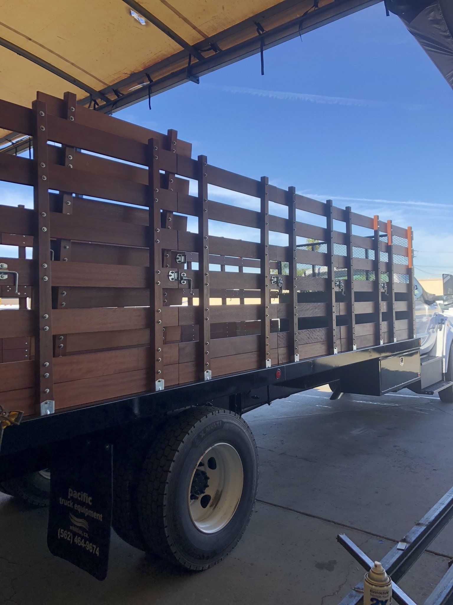 Brown wooden truck bed on a truck with black fenders and white wheels, parked under a roof.