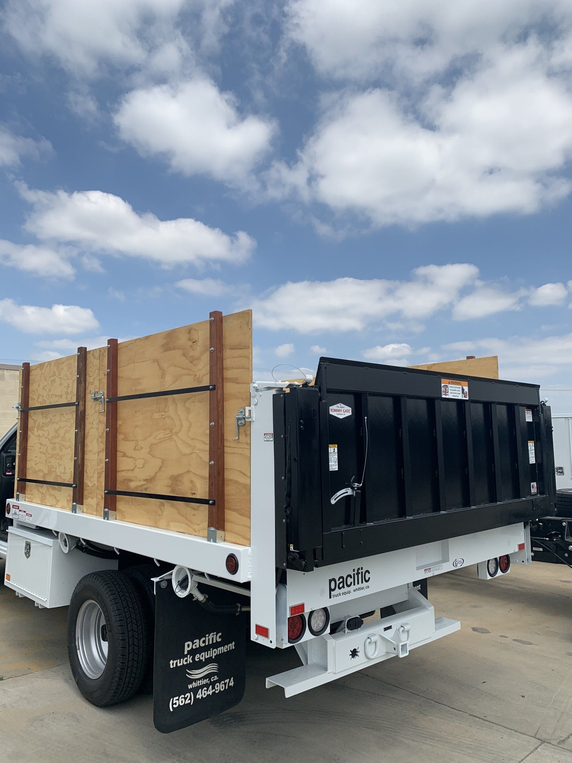White truck with black dump bed, wooden sideboards, under a cloudy sky.
