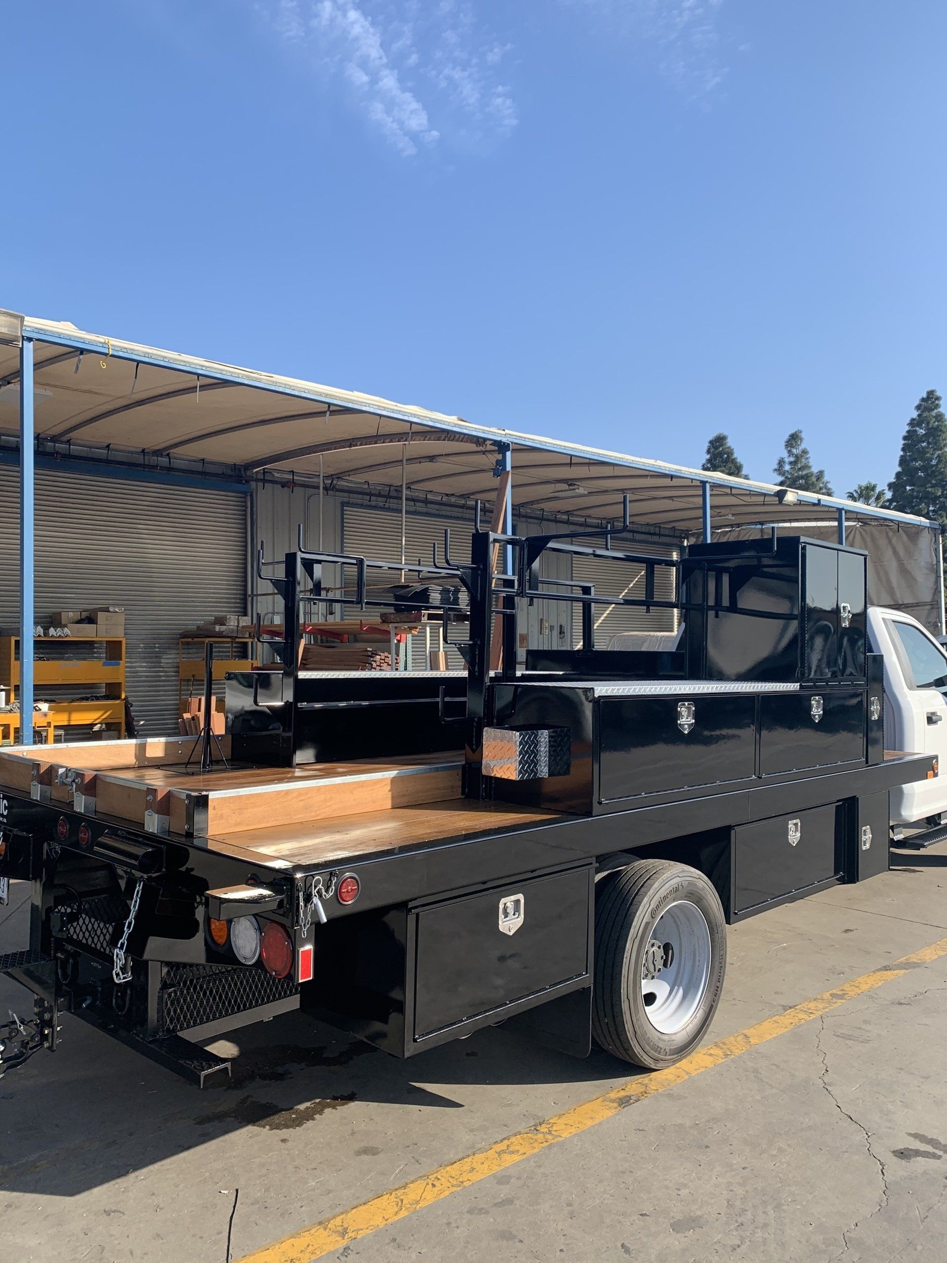 Black utility truck with flatbed and tool racks, parked outdoors.