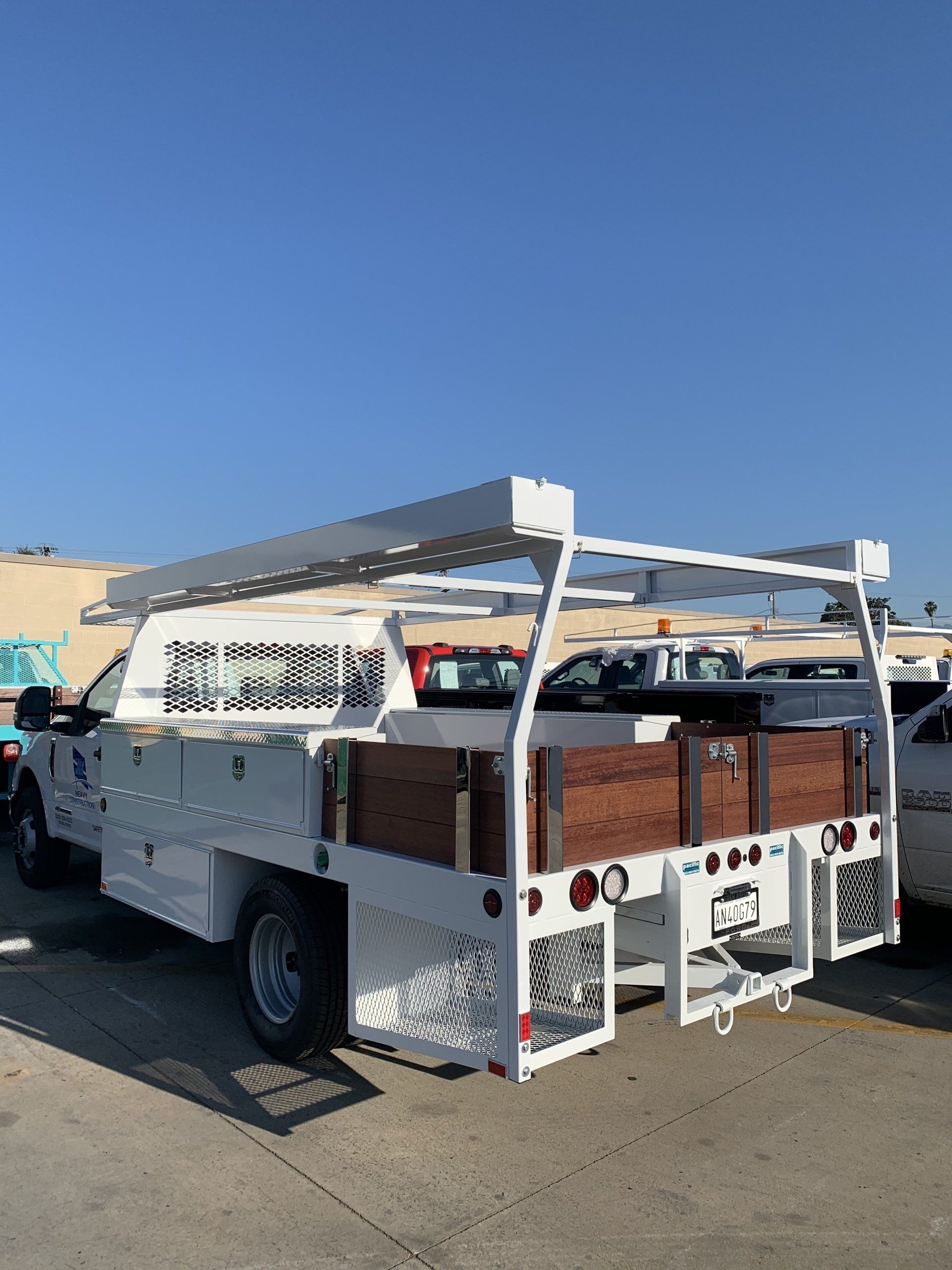 White work truck with a utility bed, wood panels, and ladder rack, parked outside on a sunny day.