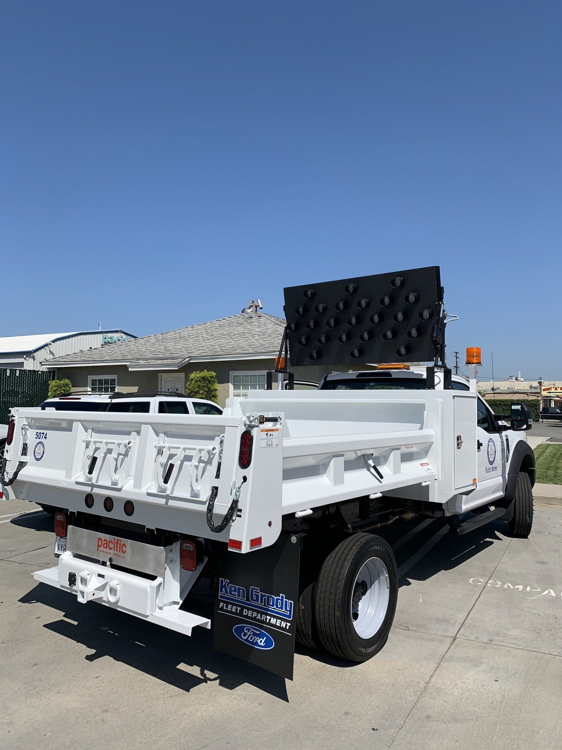 White dump truck with a large black LED sign, parked outdoors under a blue sky.