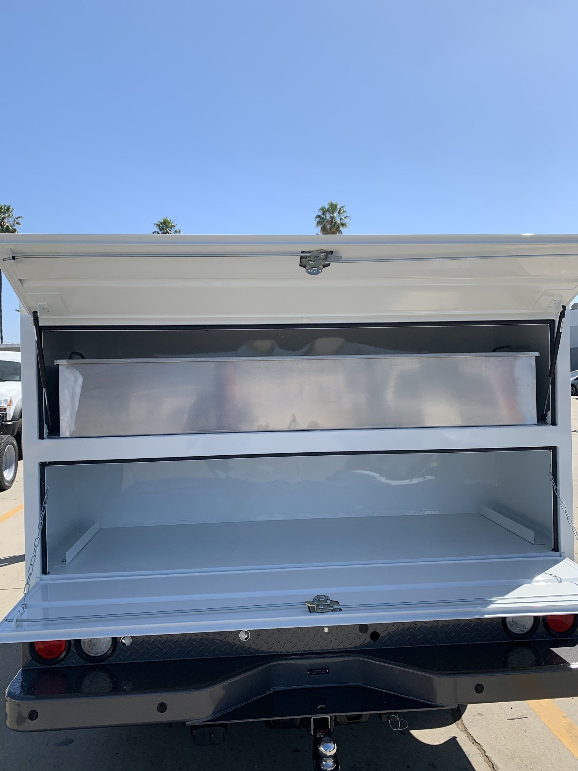 White truck bed with open hatch, revealing a shelf and storage area.