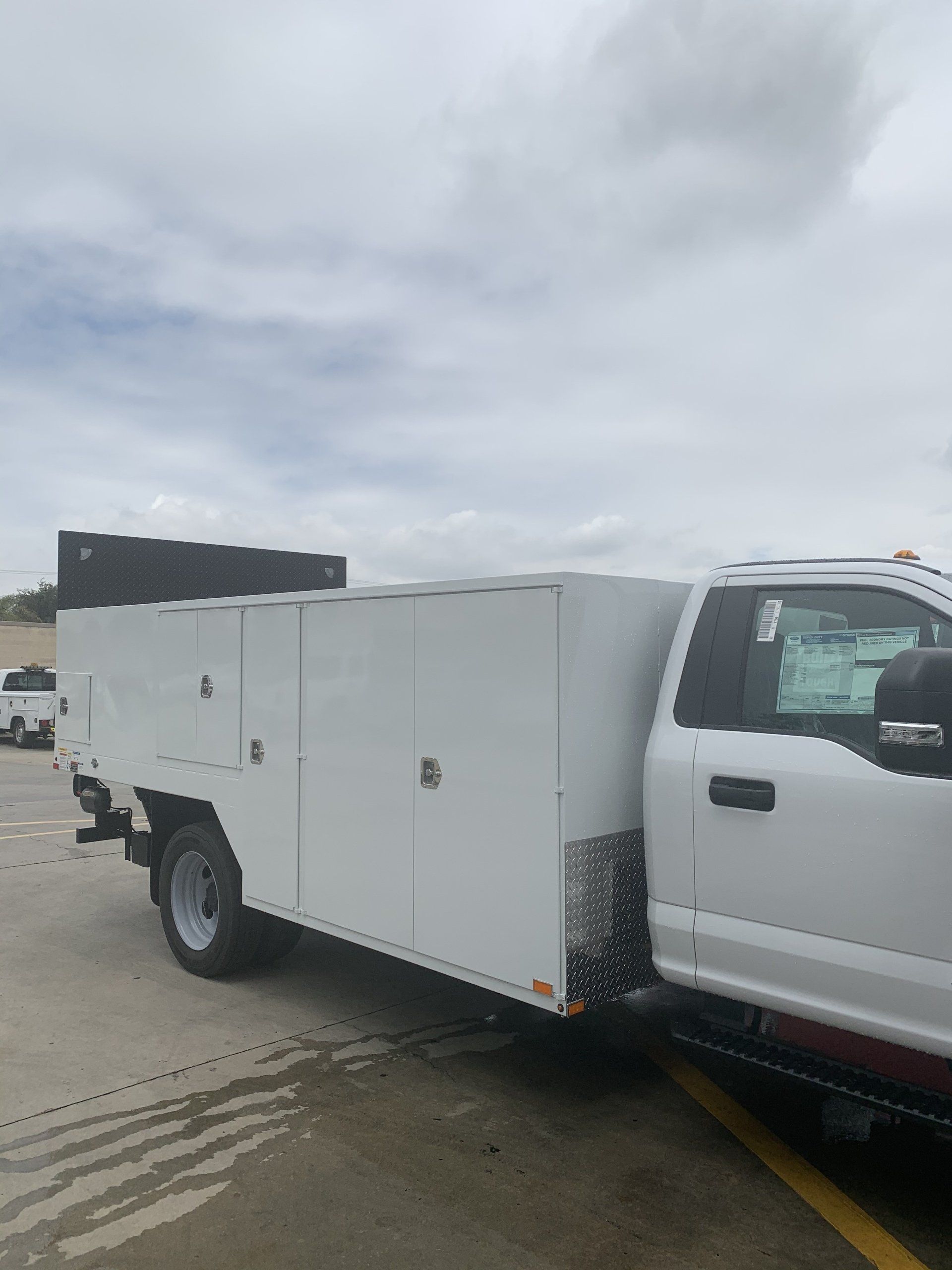 White work truck with enclosed service body parked on concrete, overcast sky.