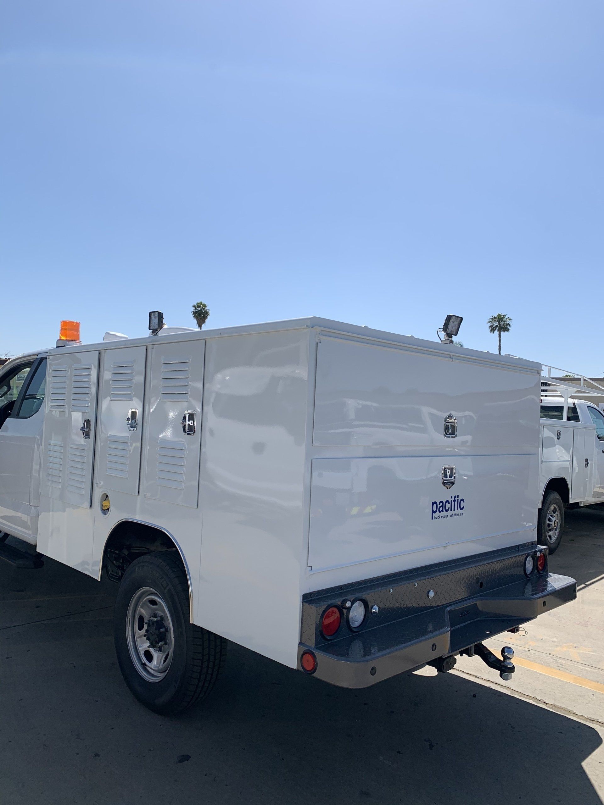 White work truck with a toolbox bed, parked outdoors under a blue sky.