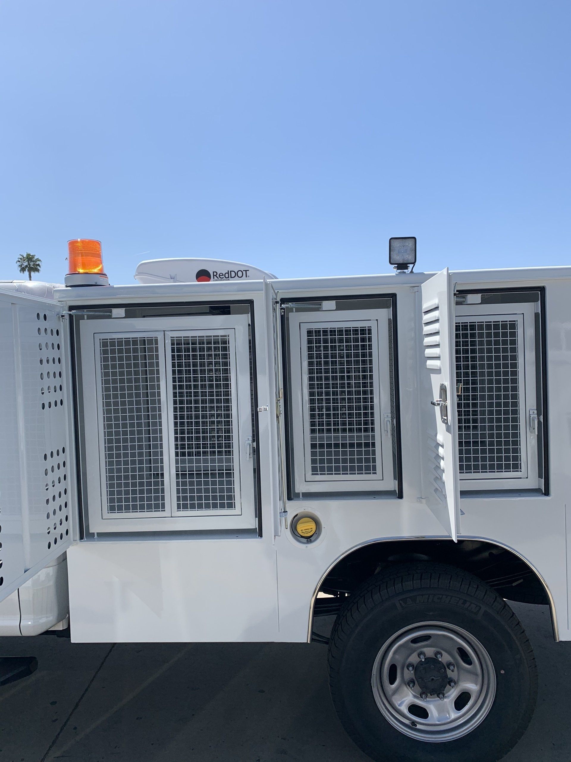 White utility truck with caged windows, under a blue sky.