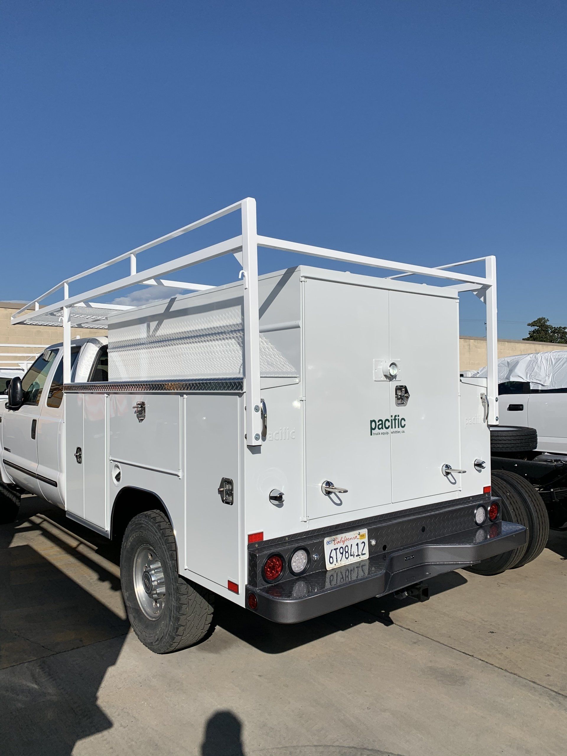 White work truck with utility bed and ladder rack parked under a clear blue sky.