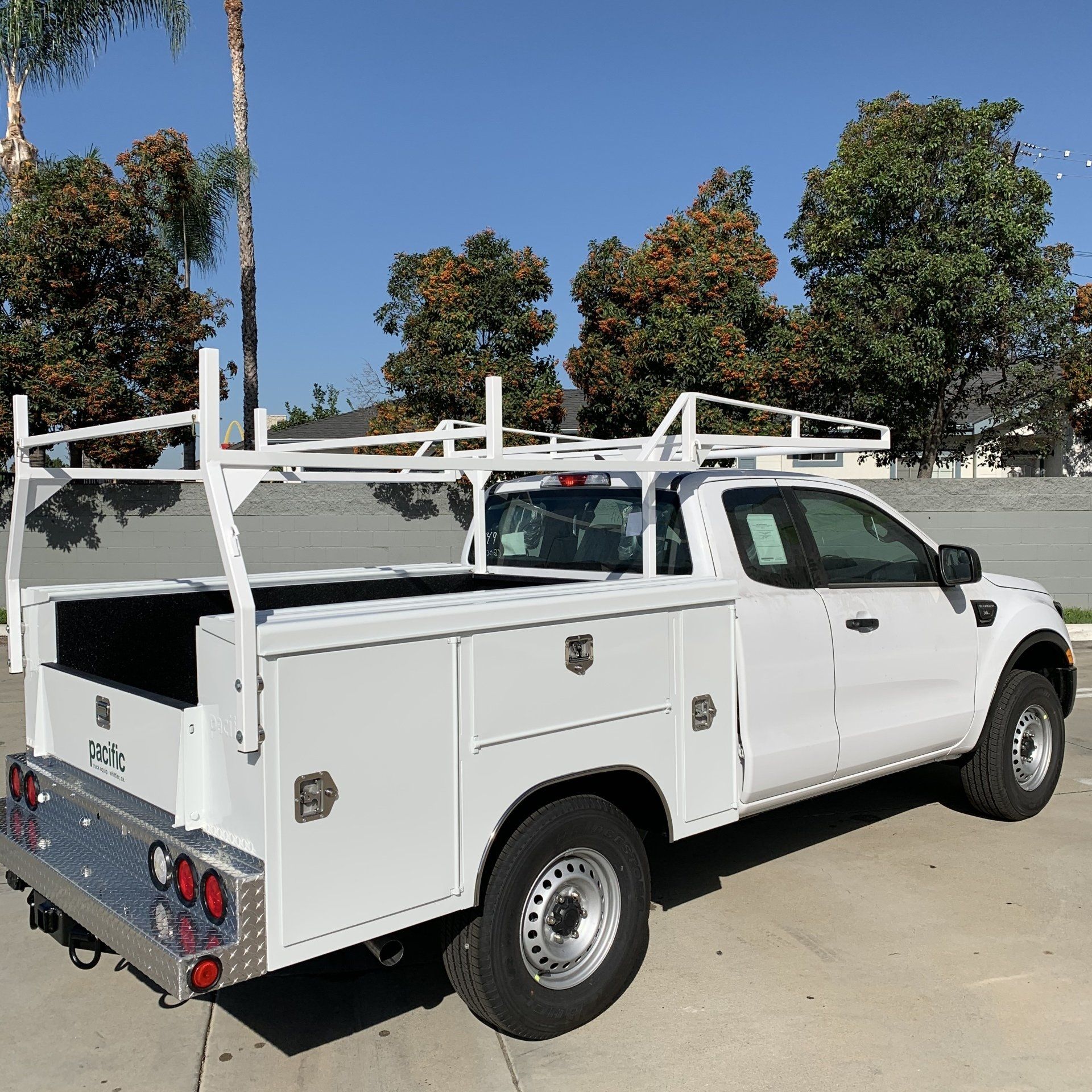 White work truck with ladder rack, toolboxes, and reflective bumper, parked outdoors.