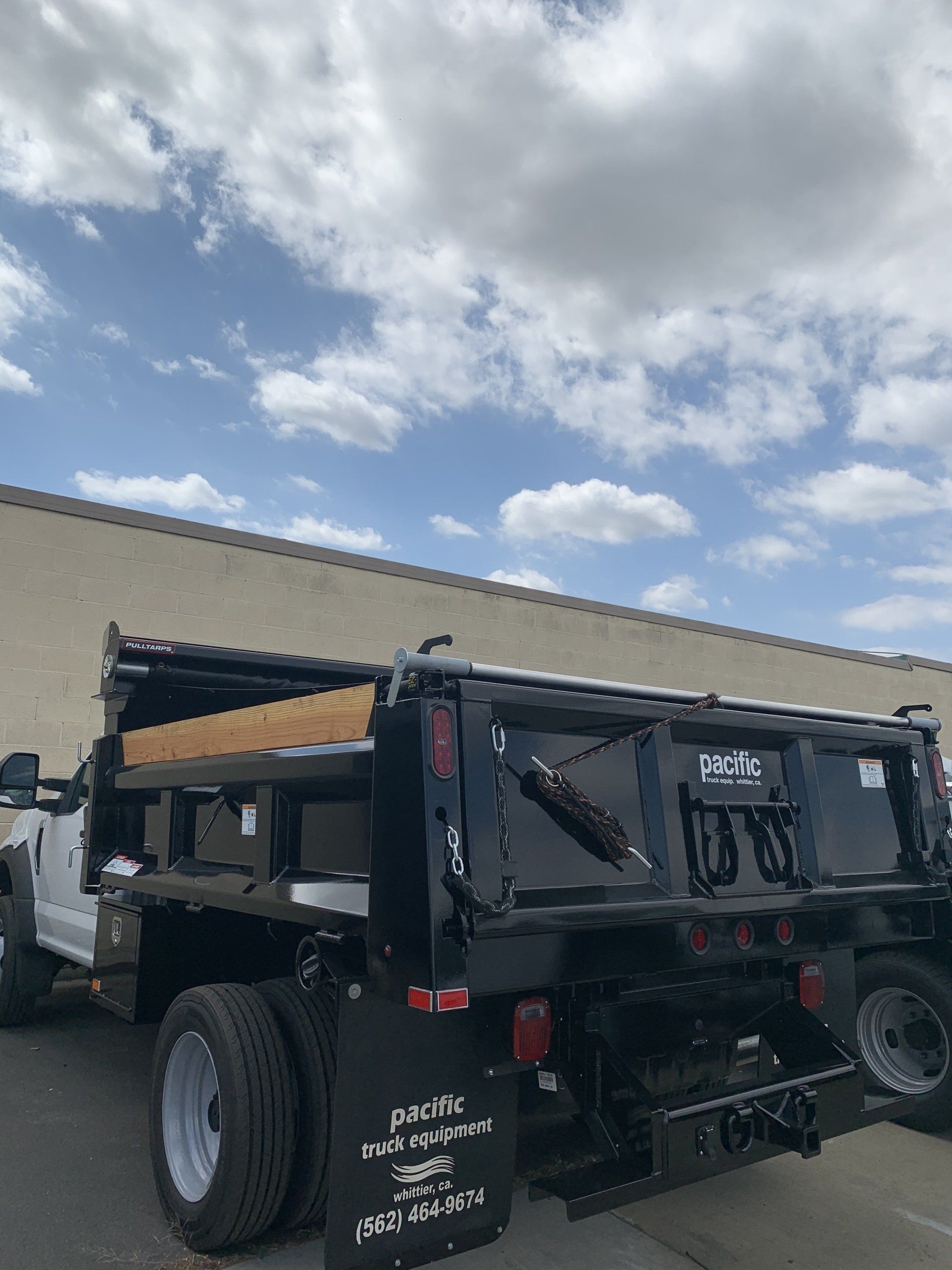 Black dump truck parked outdoors on a partly cloudy day.