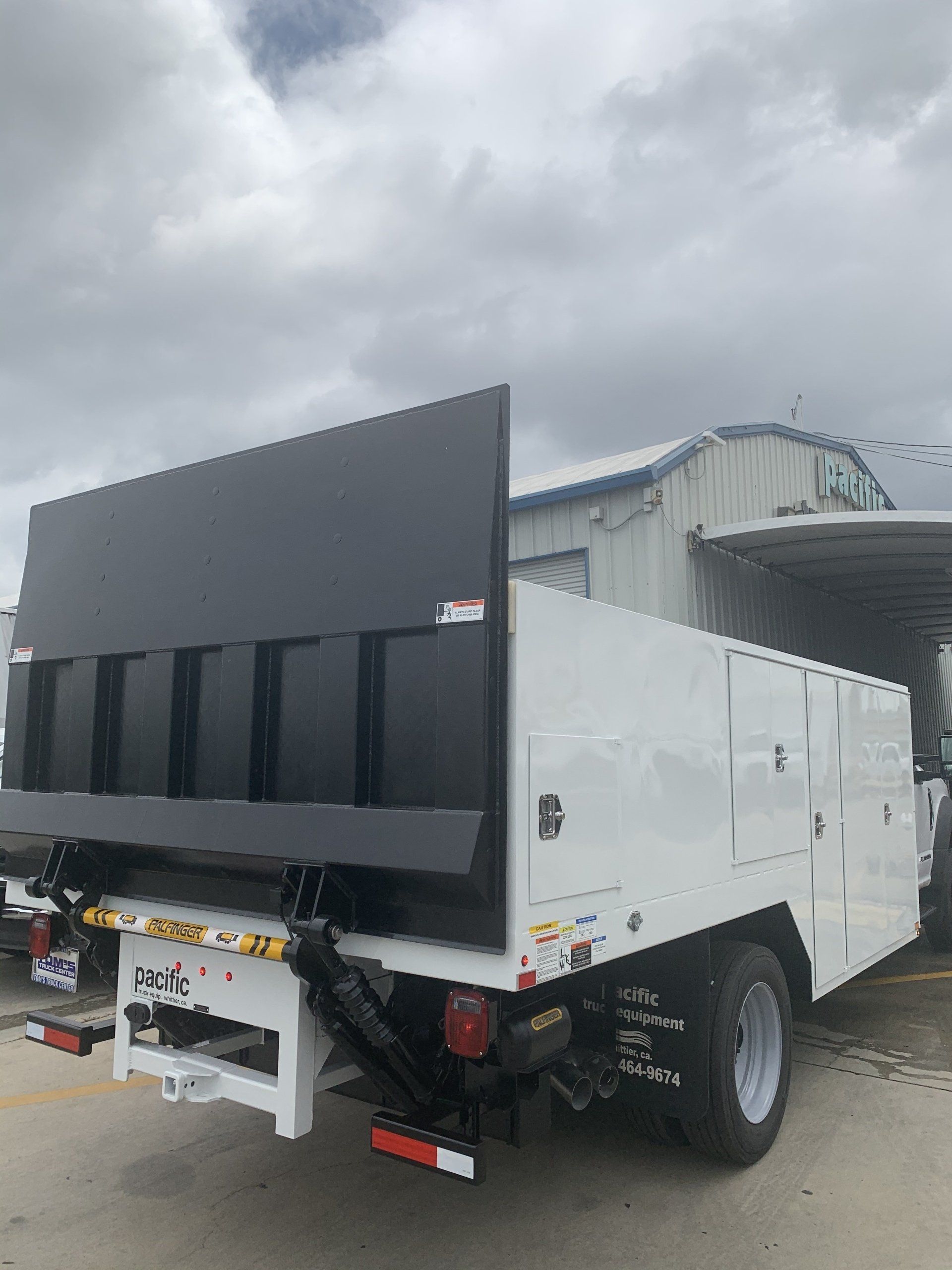 White service truck with a black tailgate in front of a building under a cloudy sky.