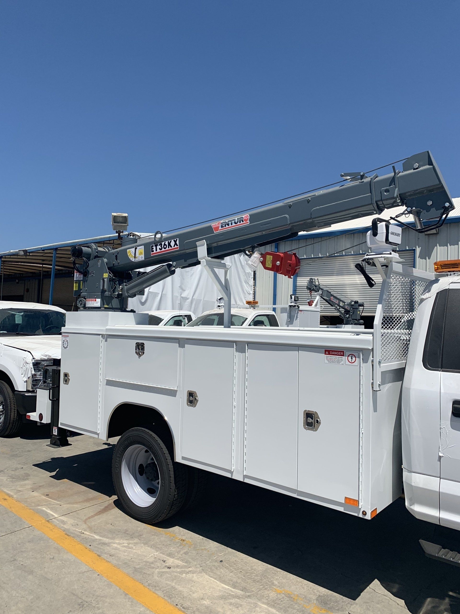 White utility truck with an extended boom under a blue sky.
