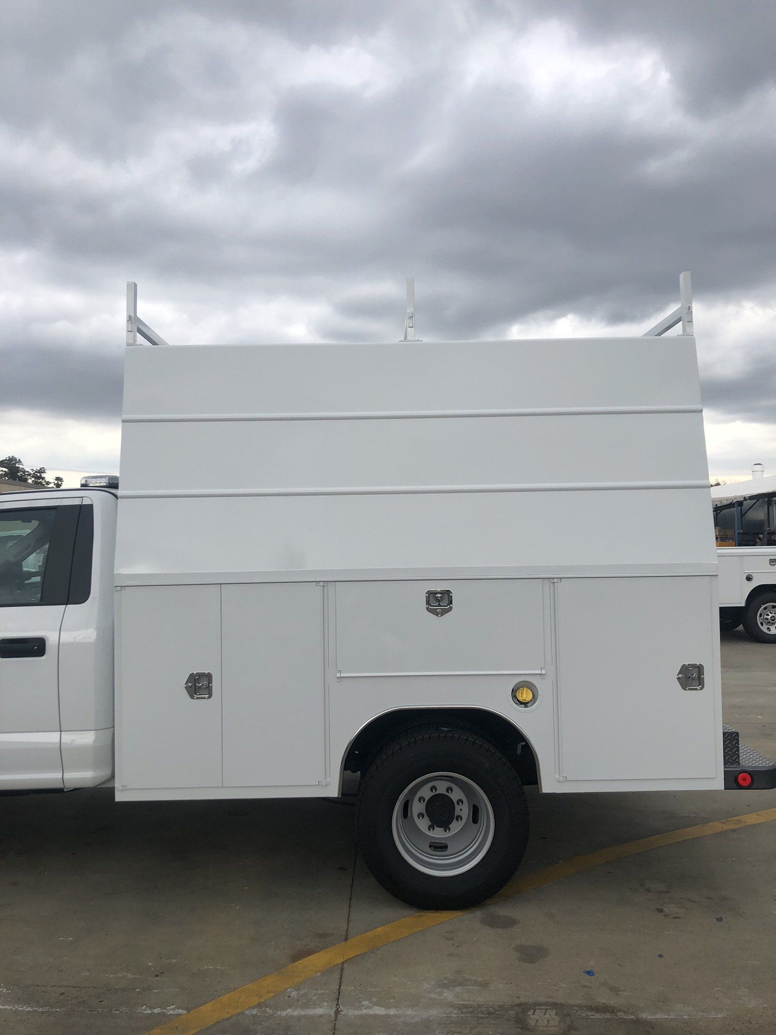 White work truck with enclosed bed, ladder racks, and storage compartments.