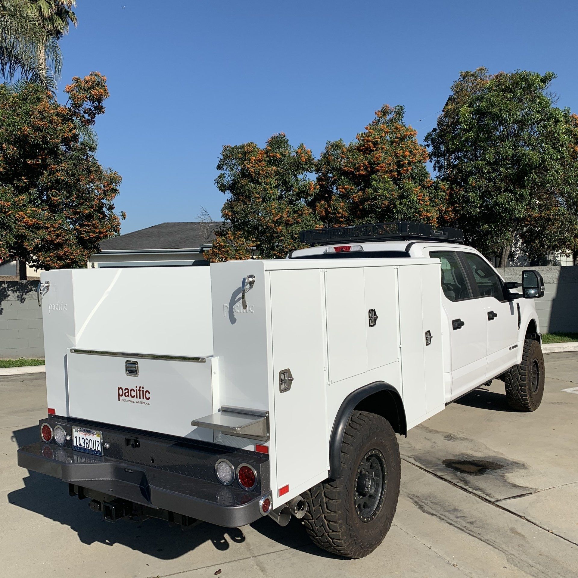 White work truck with utility bed parked on pavement, under a blue sky.