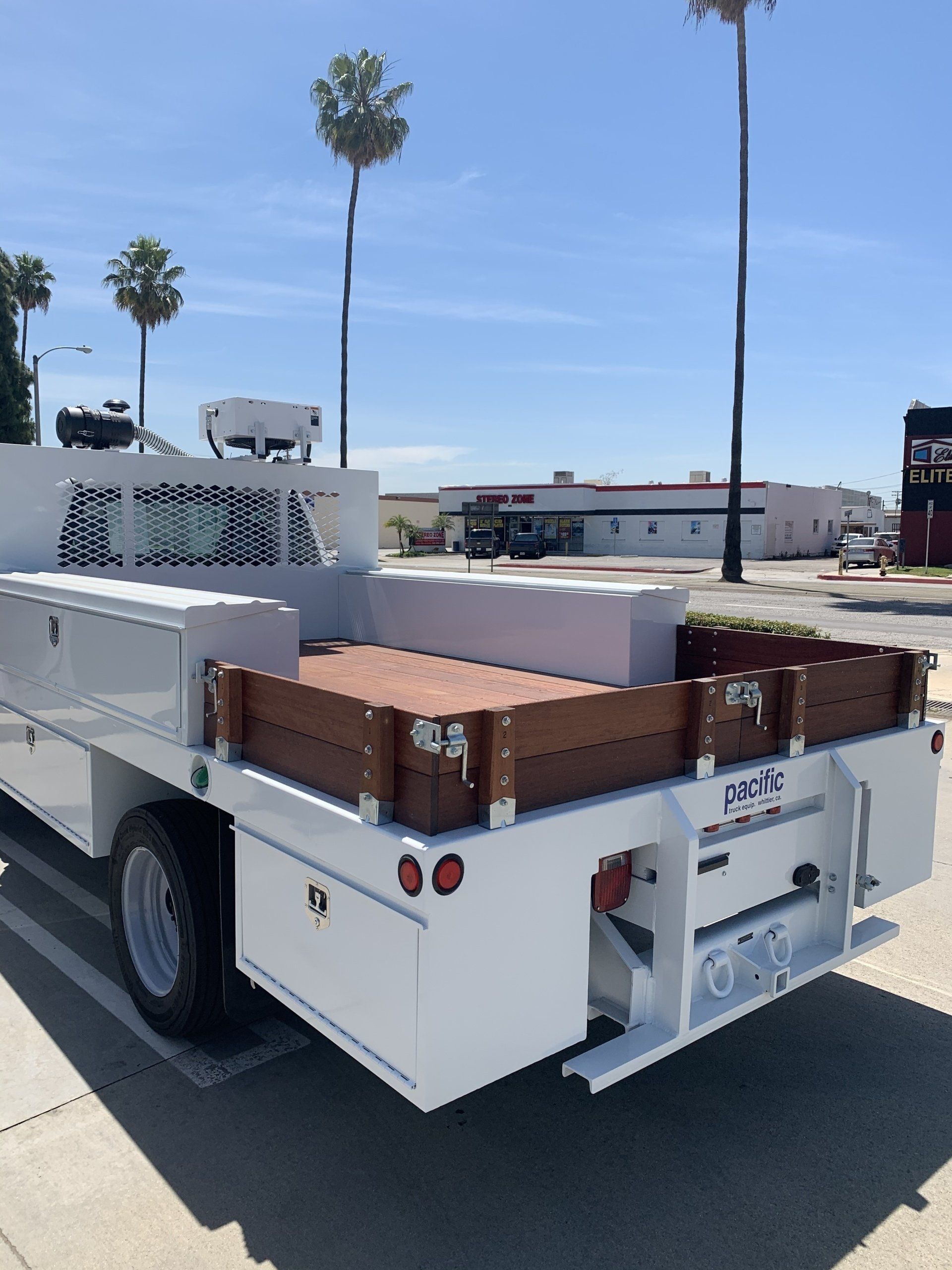 White flatbed truck with wooden bed, parked outdoors on a sunny day.
