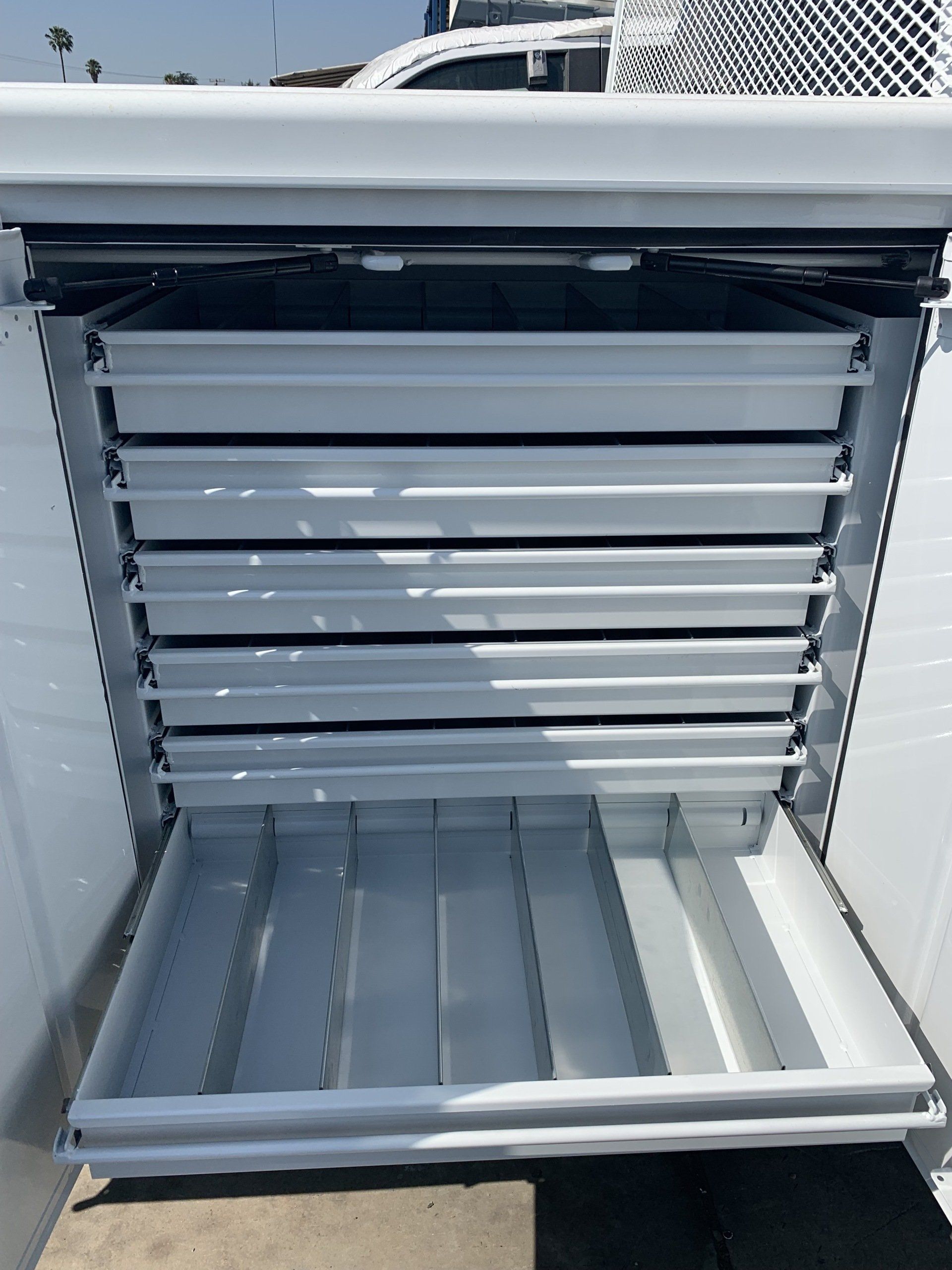 White metal tool storage cabinet with multiple open trays.