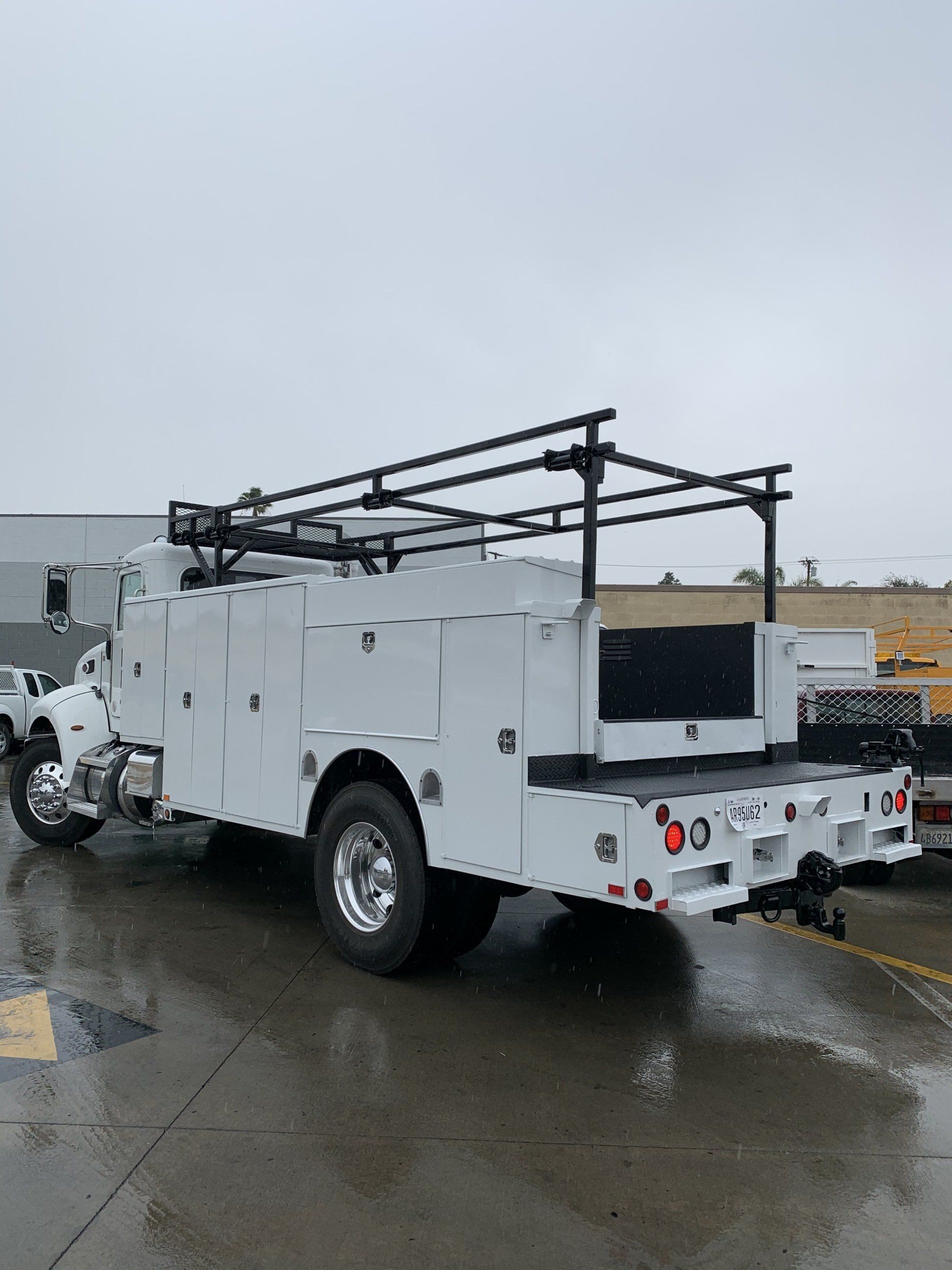 White work truck on an overcast day, with ladder rack and storage compartments.