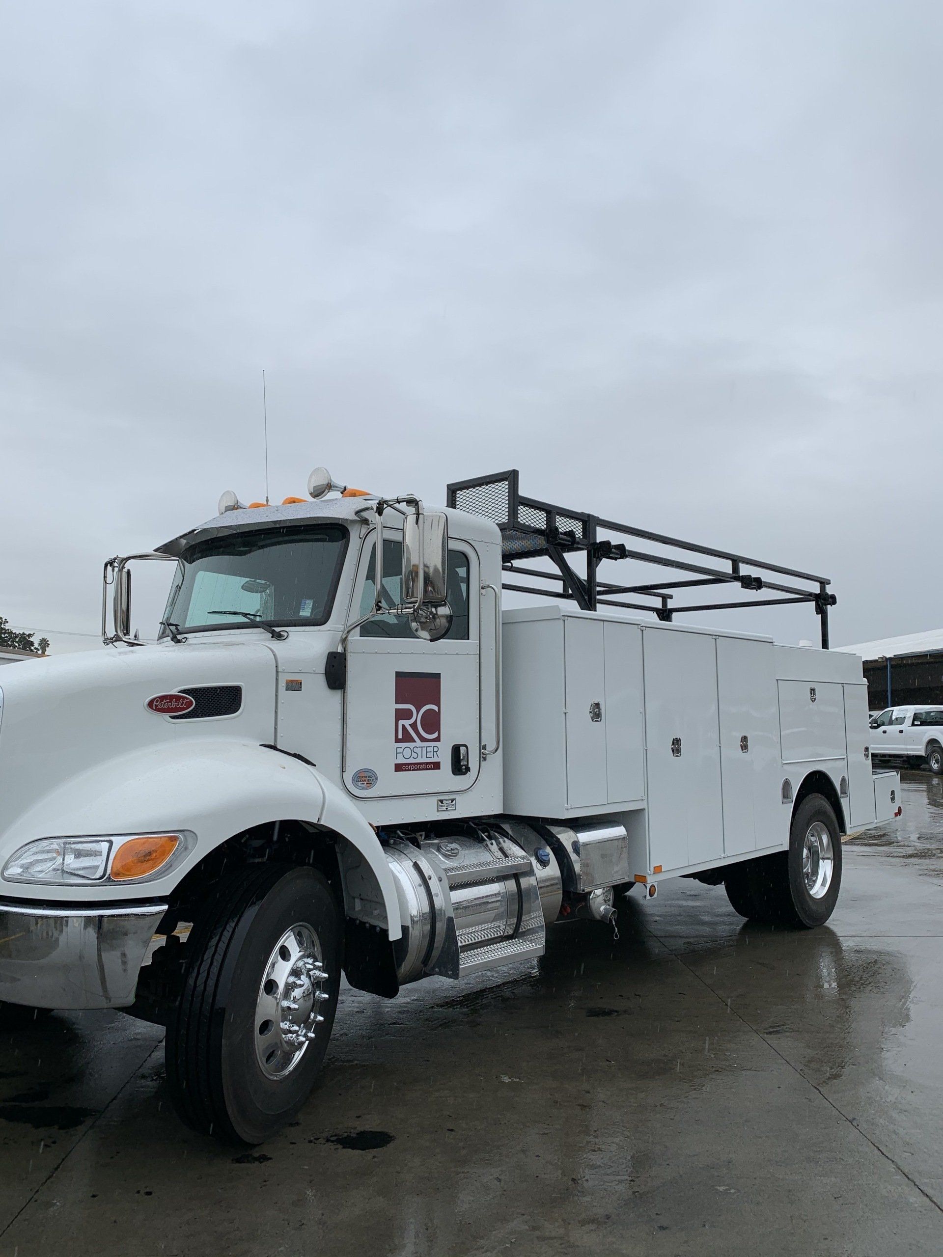 White work truck with storage compartments under an overcast sky.